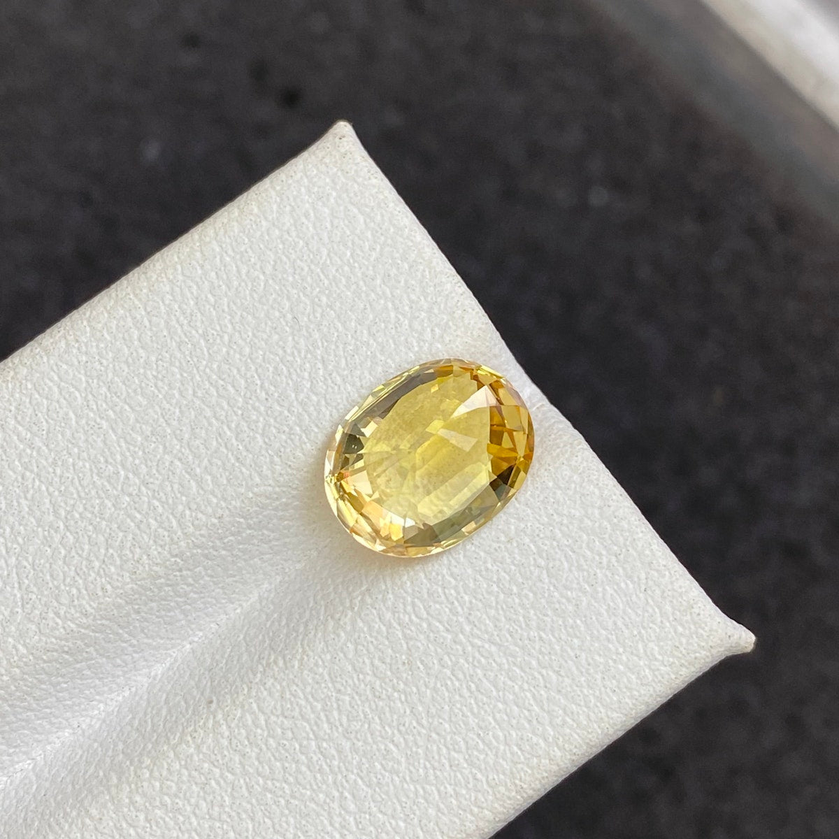 Le Saphir Jaune · 4,5 ct de Bonnot Paris est une pierre précieuse jaune polie de taille ovale présentée sur une surface blanche sur un fond sombre, avec une qualité brillante et translucide qui reflète magnifiquement la lumière.
