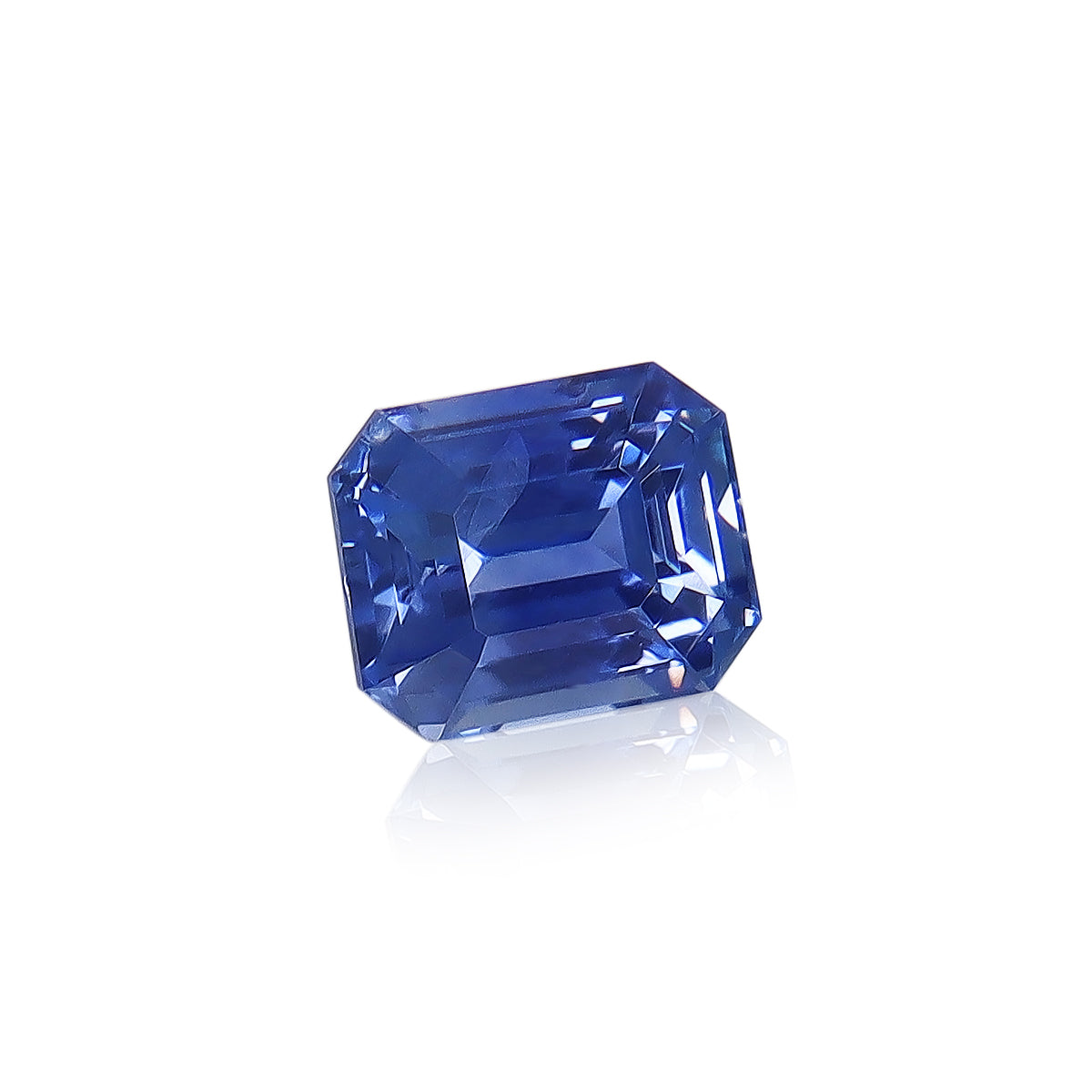 Un Saphir Bleu éclatant de 1,61 ct de Bonnot Paris, taille émeraude allongée, finement facetté et originaire du Sri Lanka. Présenté sur une surface blanche réfléchissante, il met en valeur sa transparence et sa couleur vibrante.