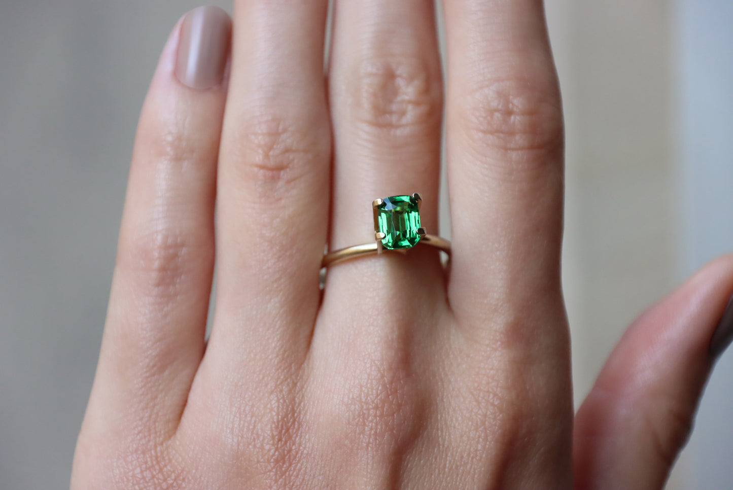 Une main soigneusement manucurée présente la bague en or Grenat Tsavorite de Bonnot Paris, sertie d'une pierre précieuse verte rectangulaire de 1,54 ct.