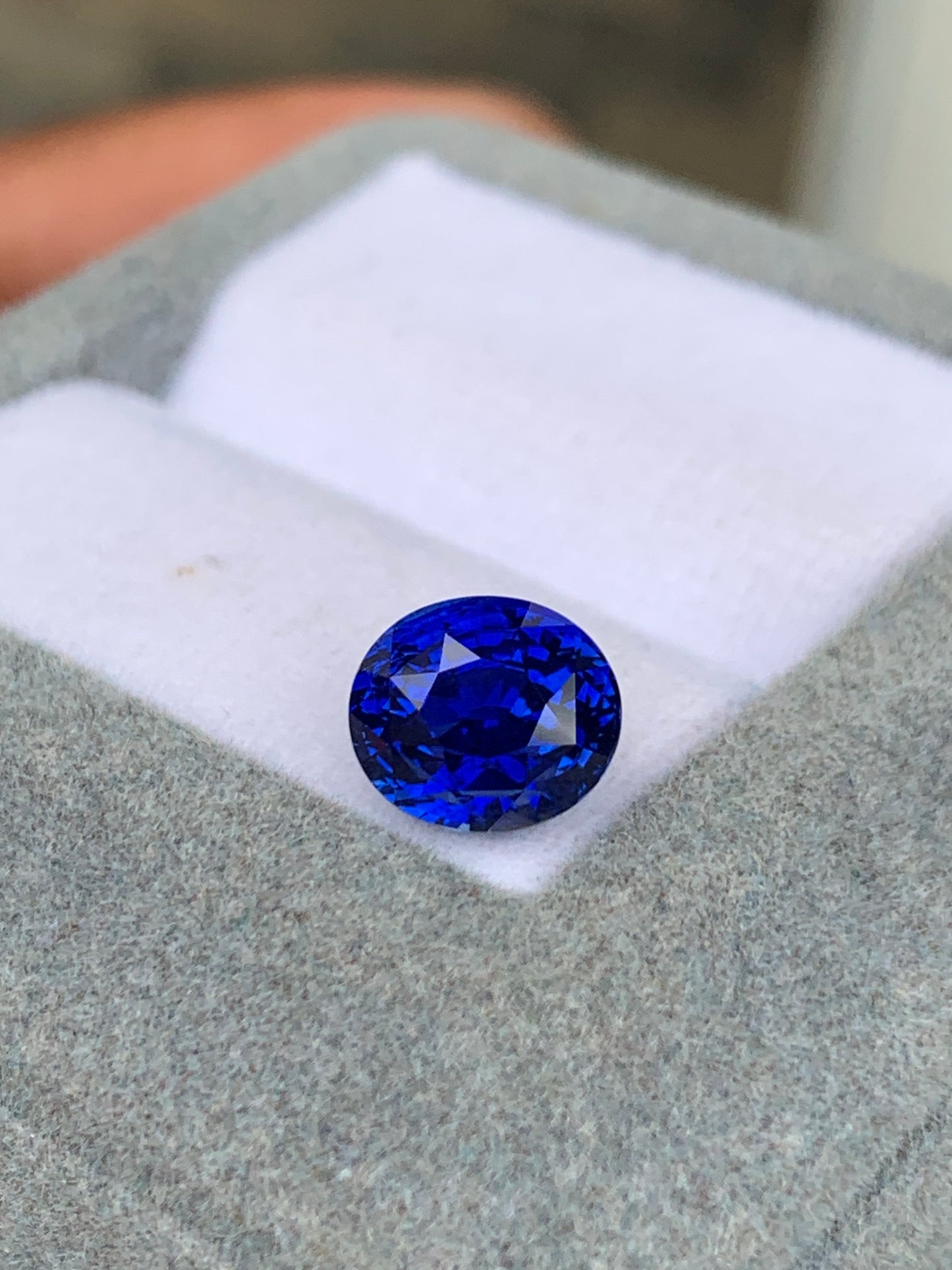 Gros plan sur une pierre précieuse ronde d'un bleu profond de Bonnot Paris, le Saphir Bleu • 3,25 carats, posée sur un écrin doublé de tissu doux. La pierre scintille de mille feux, ses facettes reflétant la lumière comme des pierres précieuses.