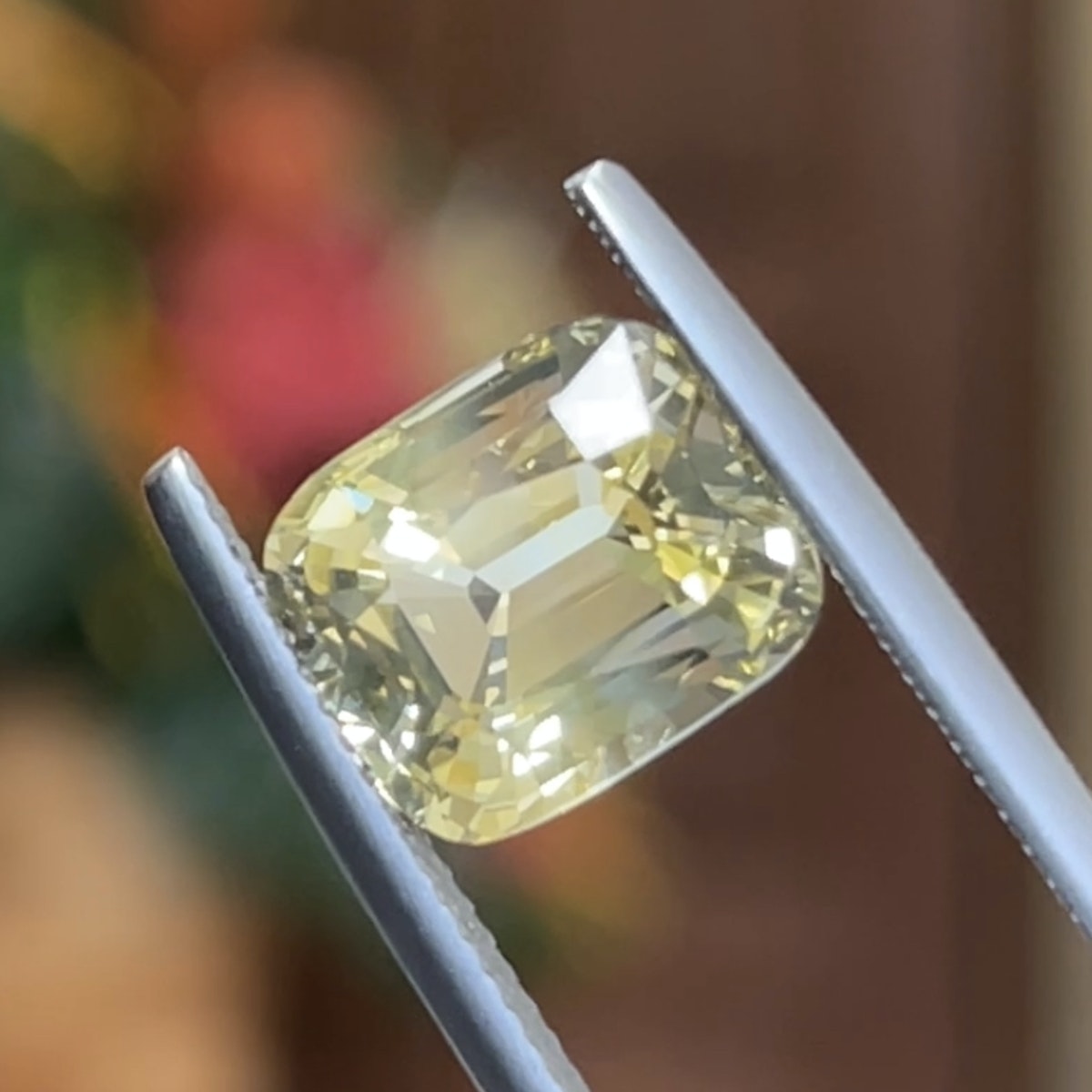 Un diamant jaune de 5,58 carats, Saphir Jaune de Bonnot Paris, est maintenu entre des pincettes avec un fond chaud flou accentuant sa clarté et sa taille.