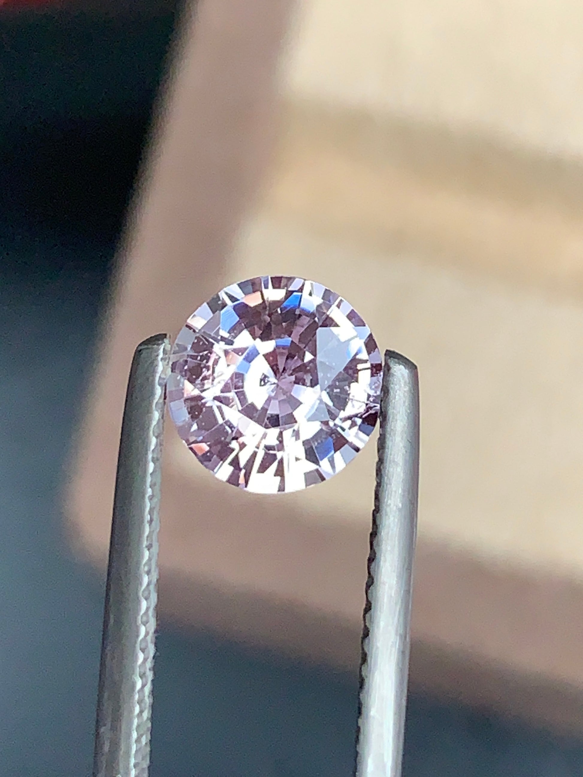 Un diamant Saphir Rose de 2,05 carats de Bonnot Paris est maintenu par une pince métallique, avec un fond doucement flou qui met en valeur son éclat et ses facettes complexes.