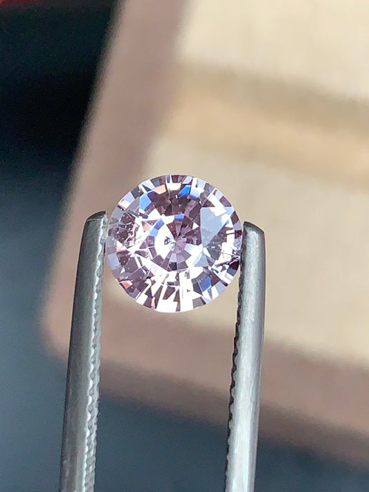 Un diamant Saphir Rose de 2,05 carats de Bonnot Paris est maintenu par une pince métallique, avec un fond doucement flou qui met en valeur son éclat et ses facettes complexes.