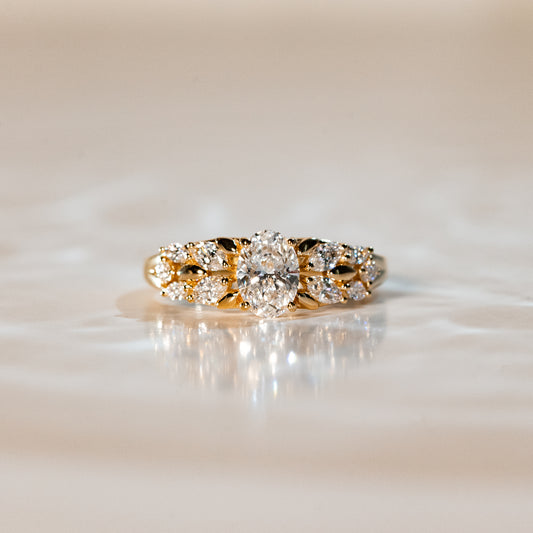 La Bague Diamants · 0,7ct de [NOUVEAU] Bonnot Paris, une bague de fiançailles en or ornée d'un diamant central flanqué de diamants plus petits, repose sur une surface réfléchissante, exsudant sophistication et élégance dans un éclairage doux.