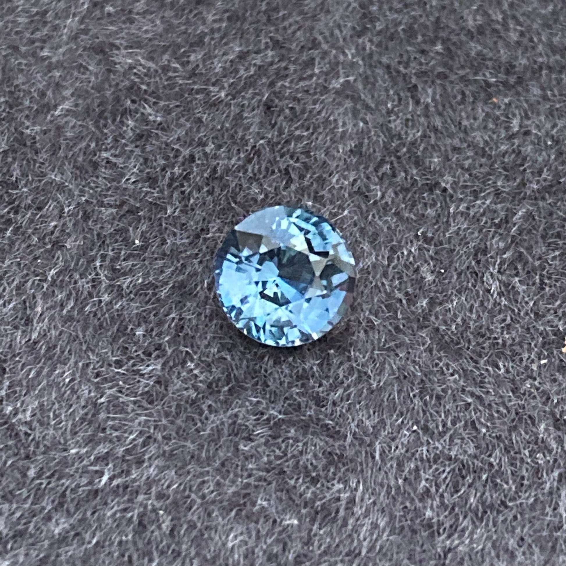 Le Saphir Teal, une pierre précieuse de 1,55 carat de Bonnot Paris, repose élégamment sur un fond texturé sombre, mettant en valeur sa beauté raffinée.