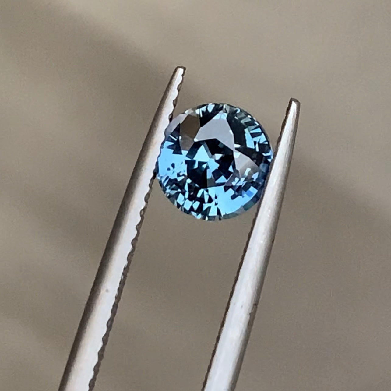 Gros plan sur le Saphir Teal de Bonnot Paris, une pierre précieuse de 1,55 carat, maintenue par une pince en argent sur un fond neutre. Il scintille de mille feux grâce à ses multiples facettes, soulignant sa clarté et sa couleur turquoise éclatante.