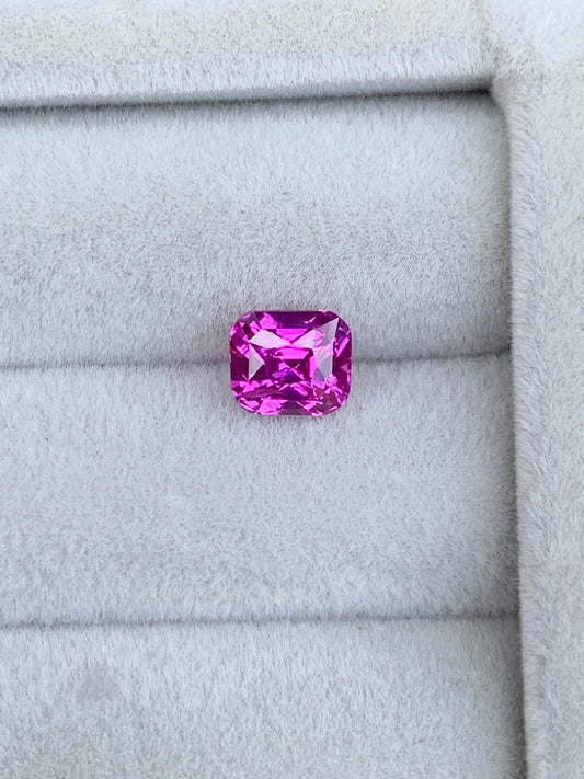Un Saphir Rose éclatant de 1,6 carat signé Bonnot Paris repose sur un tissu gris doux, avec une taille rectangulaire aux bords biseautés. Ses facettes reflètent brillamment la lumière, sublimant sa couleur vive : un véritable bijou sur mesure.