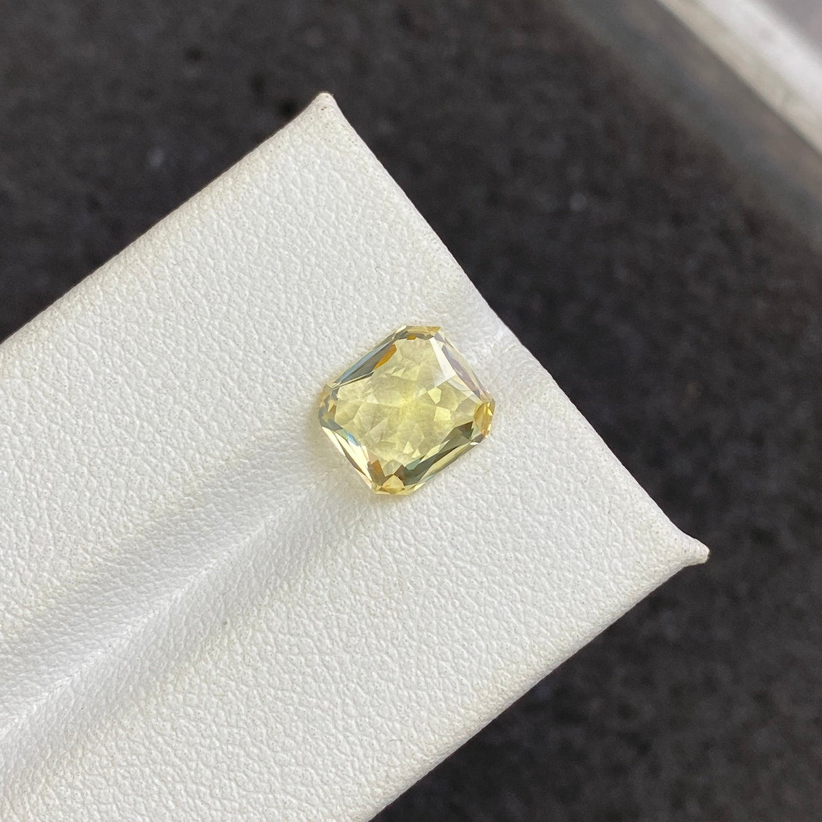 Le Saphir Jaune · 3,03ct de Bonnot Paris, une pierre précieuse jaune taille carrée, est présenté sur une surface texturée blanche avec un fond sombre et flou.