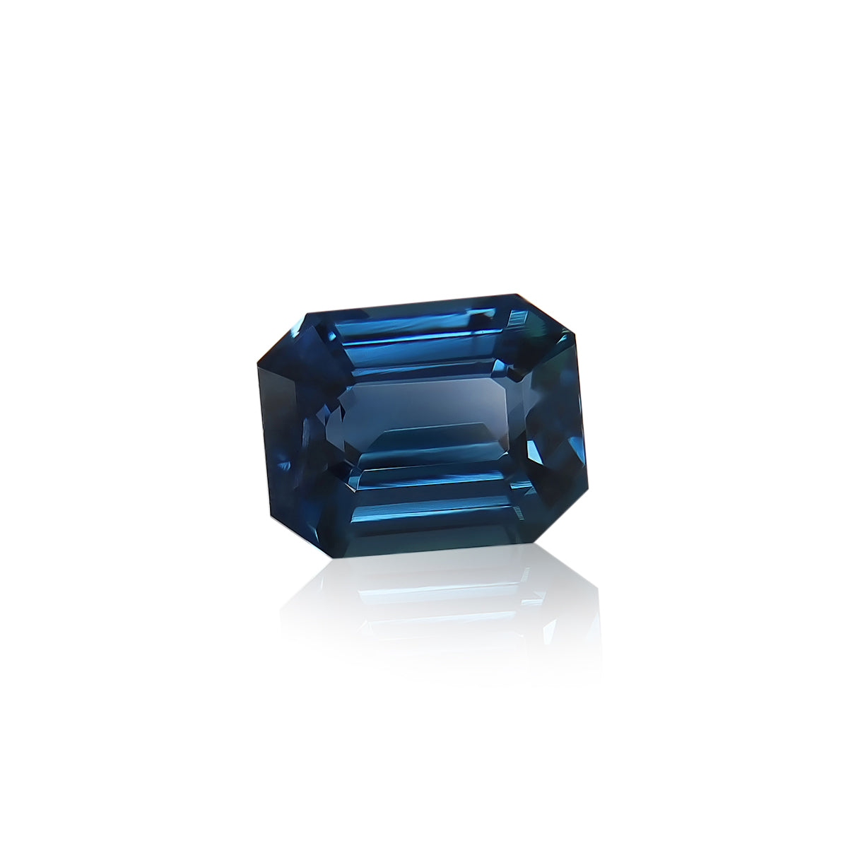 Le Saphir Teal · 2,57 ct de Bonnot Paris, une pierre précieuse taille émeraude provenant de Madagascar, présente des facettes nettes et des surfaces réfléchissantes sur un fond blanc, révélant de superbes nuances de bleu foncé et des touches de sarcelle.