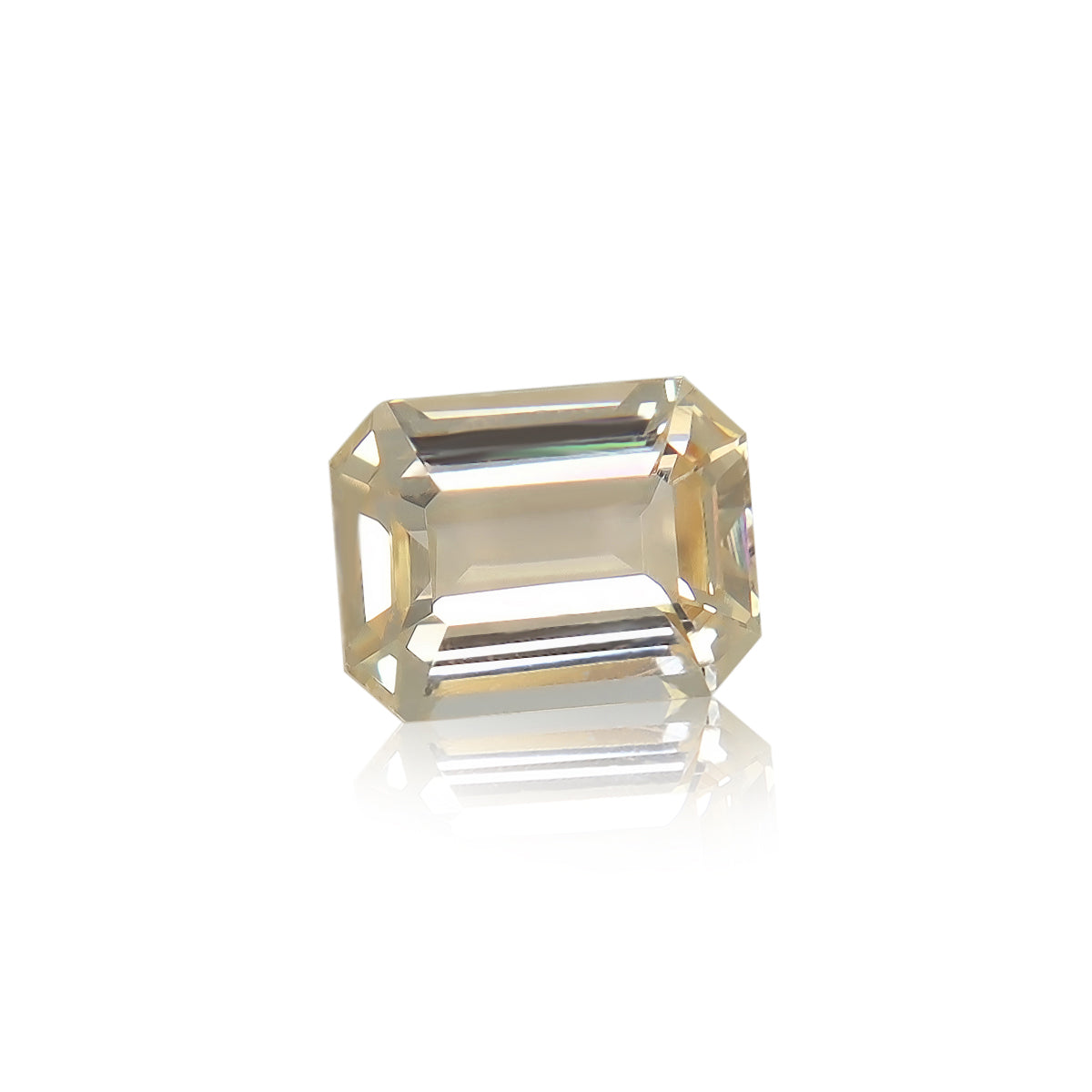 Le Saphir Orange · 1,82 carat de Bonnot Paris, une pierre rectangulaire transparente aux bords biseautés, repose sur une surface blanche réfléchissante. Ses teintes jaune clair transparentes et ses facettes scintillent sous une lumière vive, évoquant de magnifiques bijoux sur mesure.