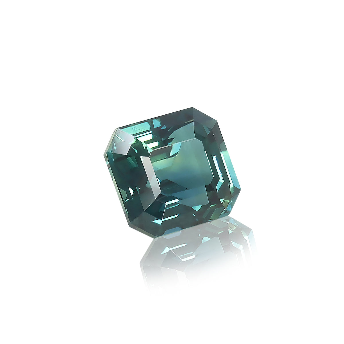 Le Saphir Teal · 3,03 ct de Bonnot Paris, une pierre précieuse taille émeraude avec une teinte bleu-vert profond, repose sur une surface blanche réfléchissante, mettant en valeur son design facetté et sa brillance vibrante.
