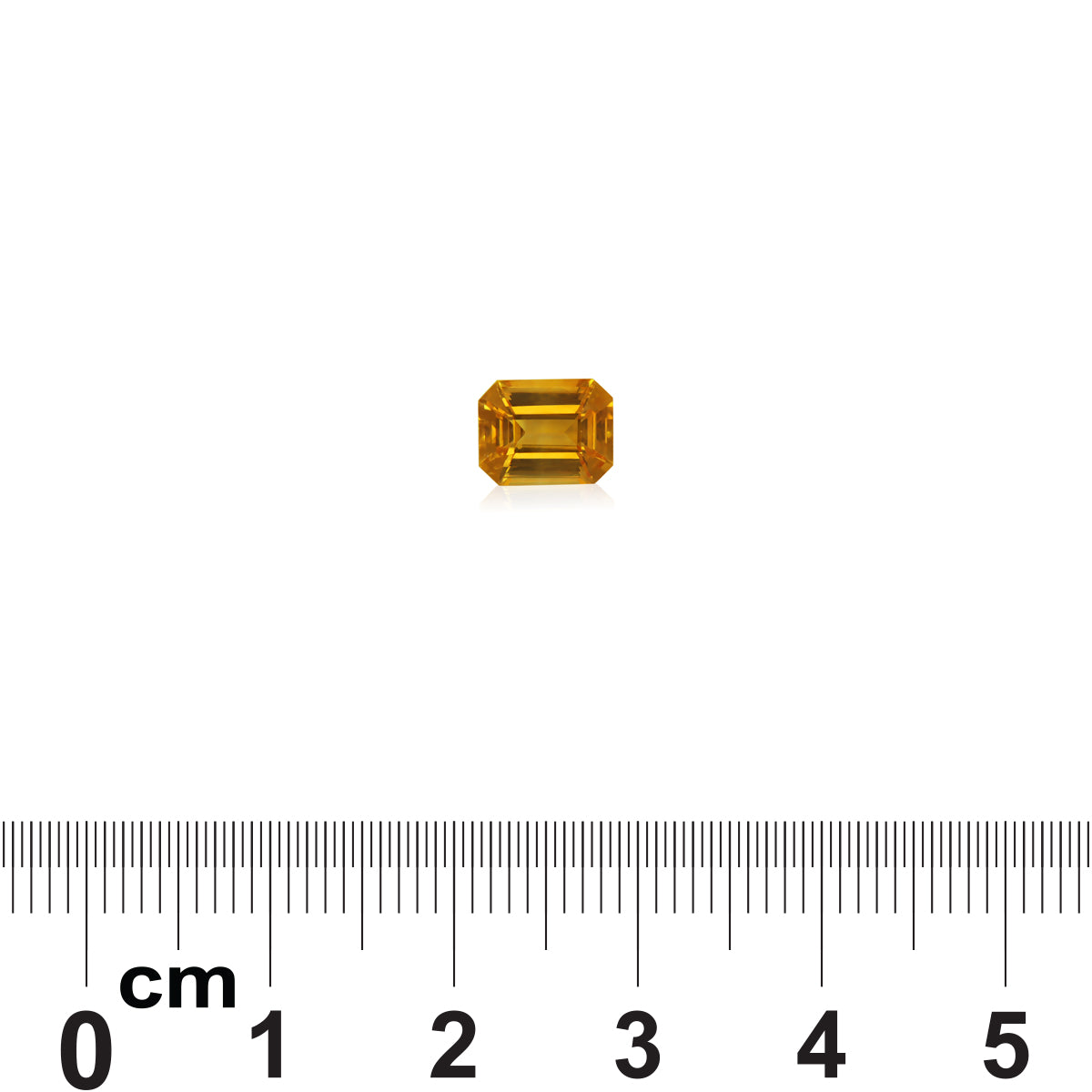 Un Saphir Jaune de 1,58 carat de Bonnot Paris, taille petite émeraude, est placé au-dessus d'une règle graduée. La teinte jaune de la pierre précieuse se reflète élégamment en dessous.