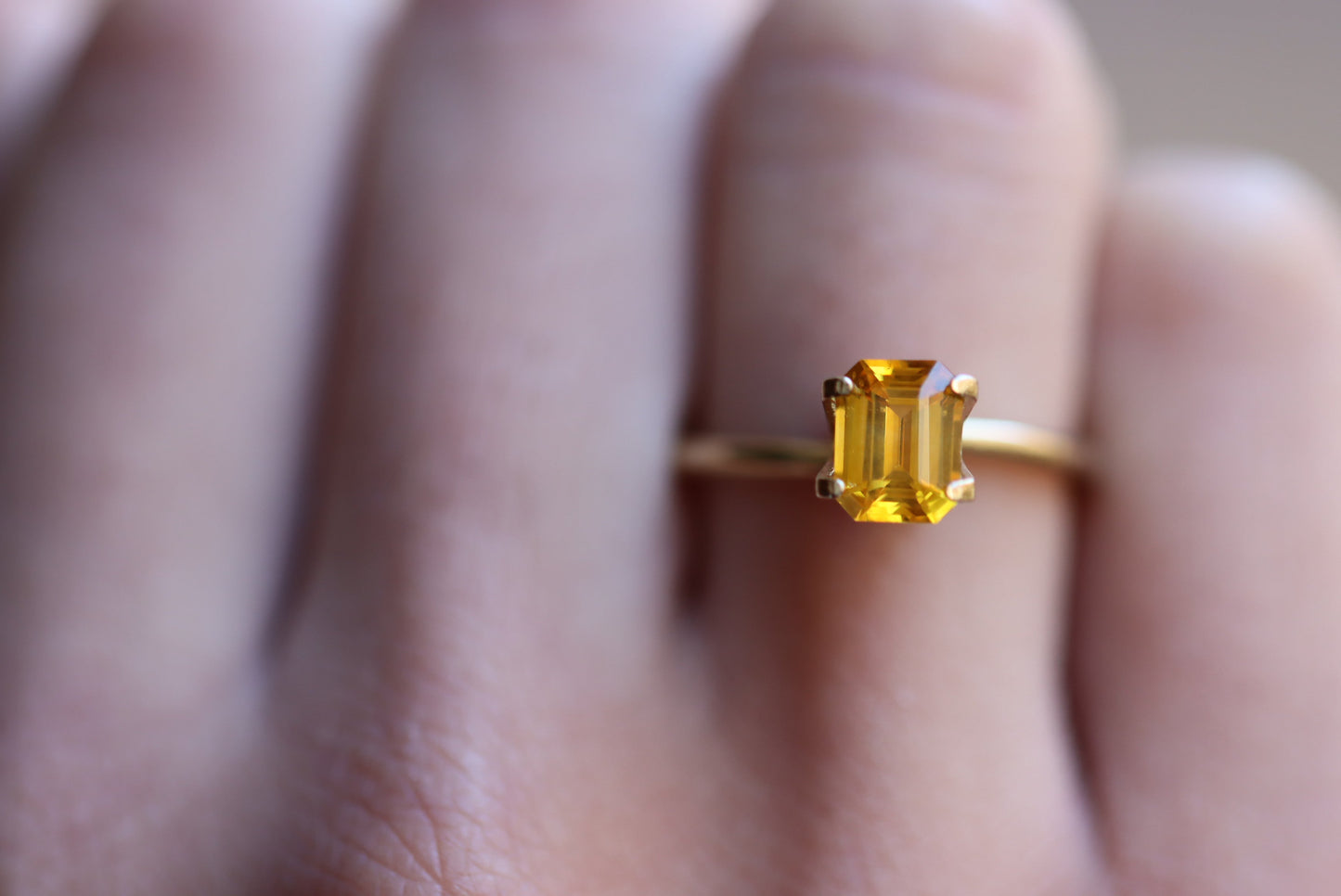 Une main présente une bague en or Bonnot Paris avec un Saphir Jaune de 1,58 ct, rappelant la gemme jaune vibrante du Sri Lanka, volant l'attention sur un arrière-plan flou.