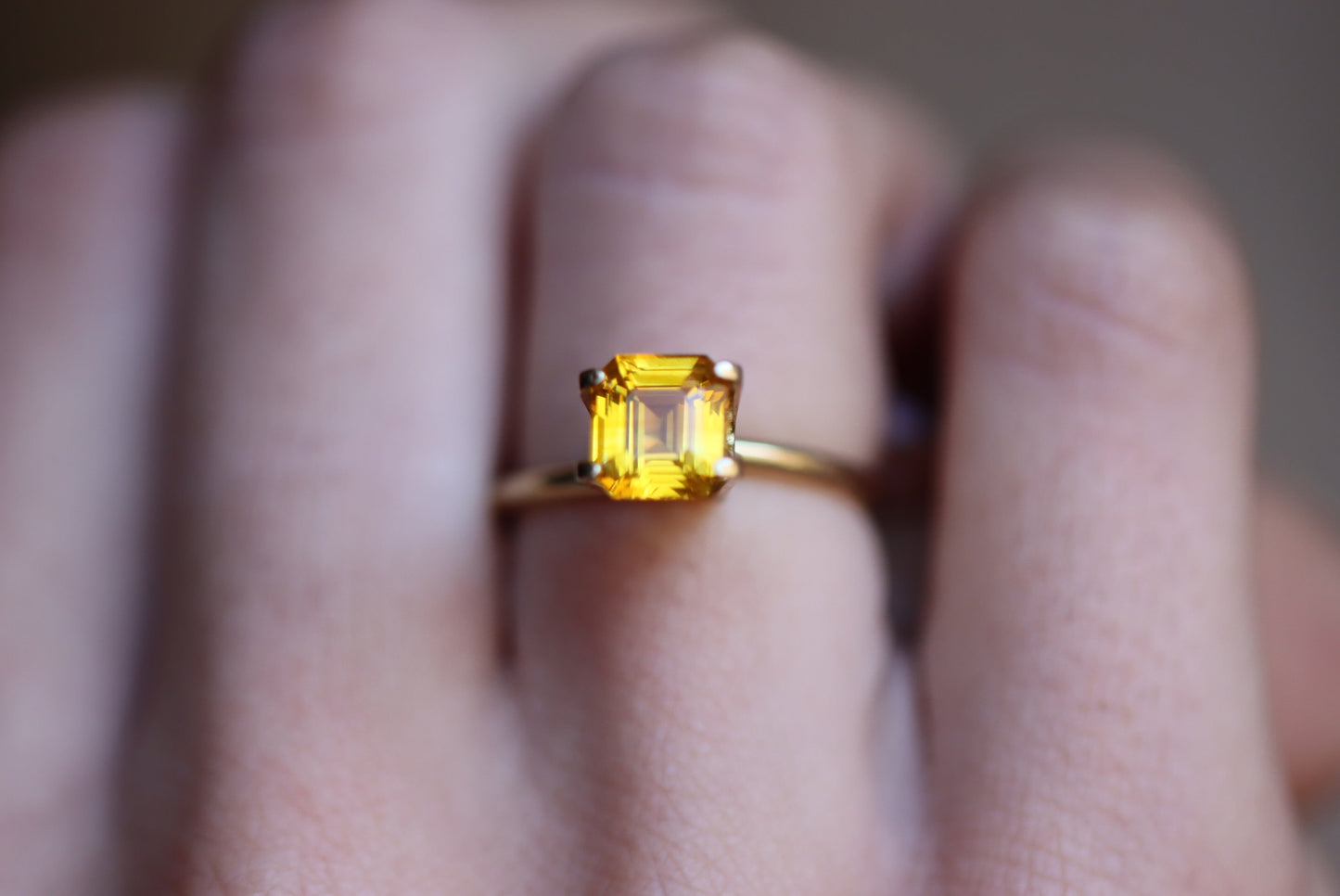 Une main met en valeur la bague Saphir Jaune · 2,04 ct de Bonnot Paris, comportant une pierre précieuse jaune taille carrée proéminente sertie d'or sur un fond flou.