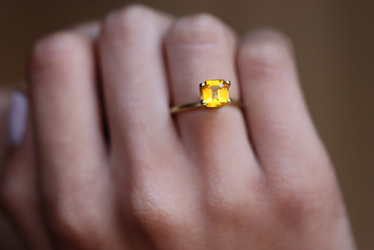 Une main portant la bague en or Saphir Jaune · 2,04 carats de Bonnot Paris avec une pierre précieuse jaune rectangulaire facettée sur un fond flou, soulignant la couleur vibrante de la bague et son sertissage élégant.