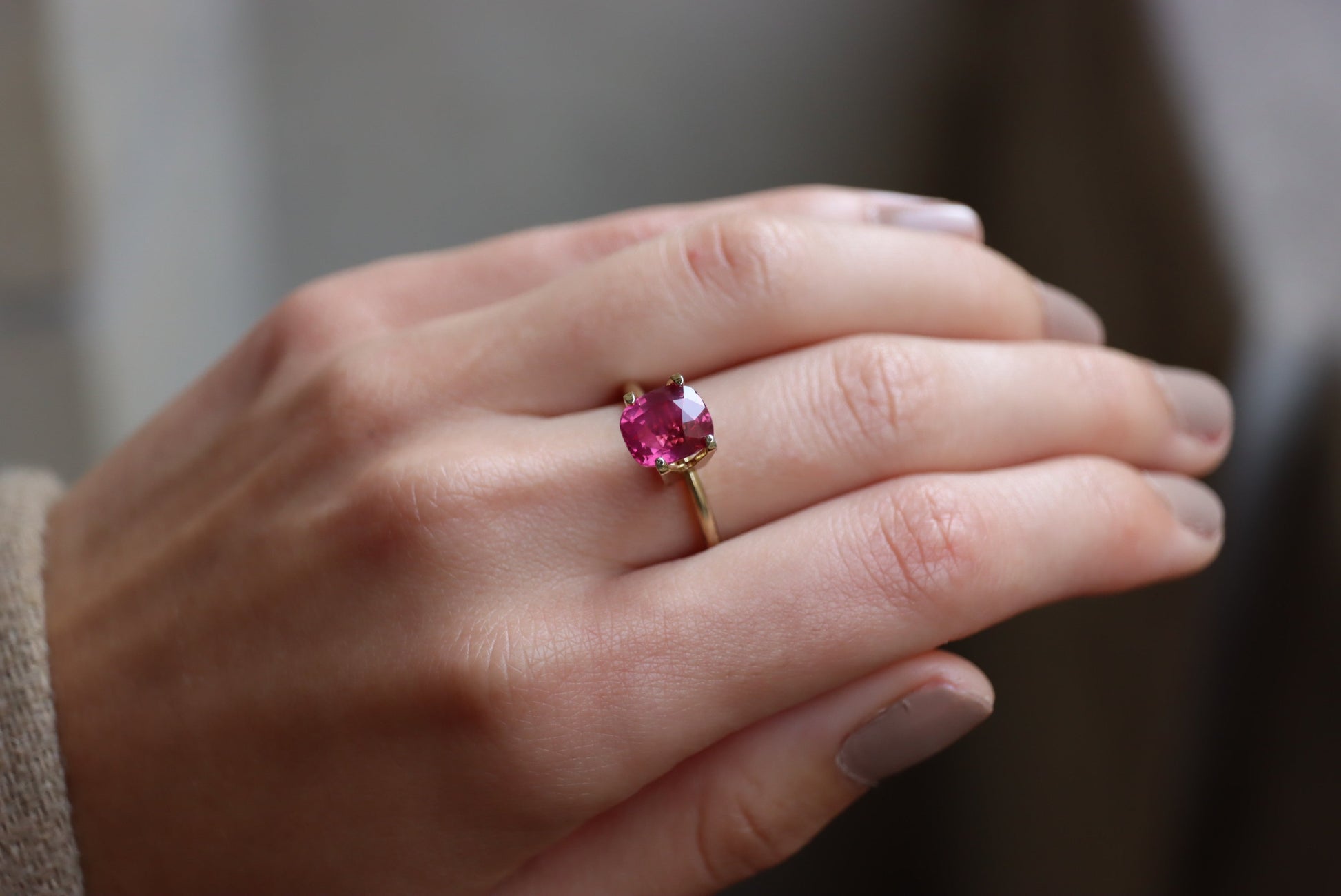 Gros plan d'une main ornée du Saphir Rose · 3,02 carats de Bonnot Paris, mettant en valeur une grosse pierre ronde rose vif. La main est ornée d'un vernis à ongles de couleur neutre sur un arrière-plan légèrement flou.