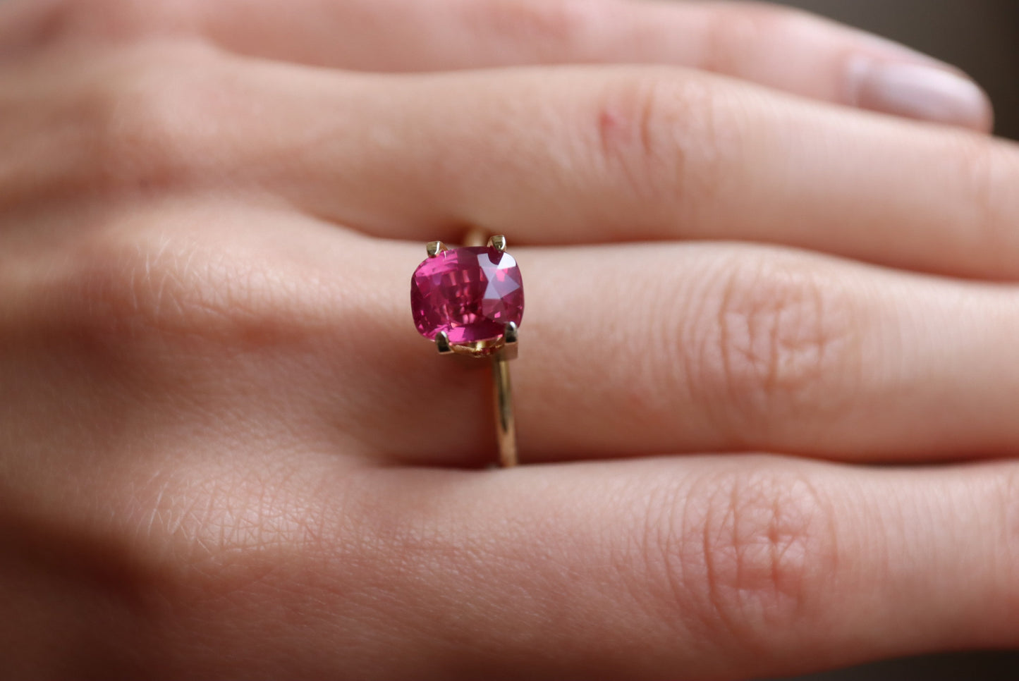 Gros plan sur une main ornée du Saphir Rose de Bonnot Paris, une bague en or ornée d'une pierre rose vif facettée de 3,02 carats. Cette pierre capte magnifiquement la lumière, mettant en valeur sa teinte vibrante.