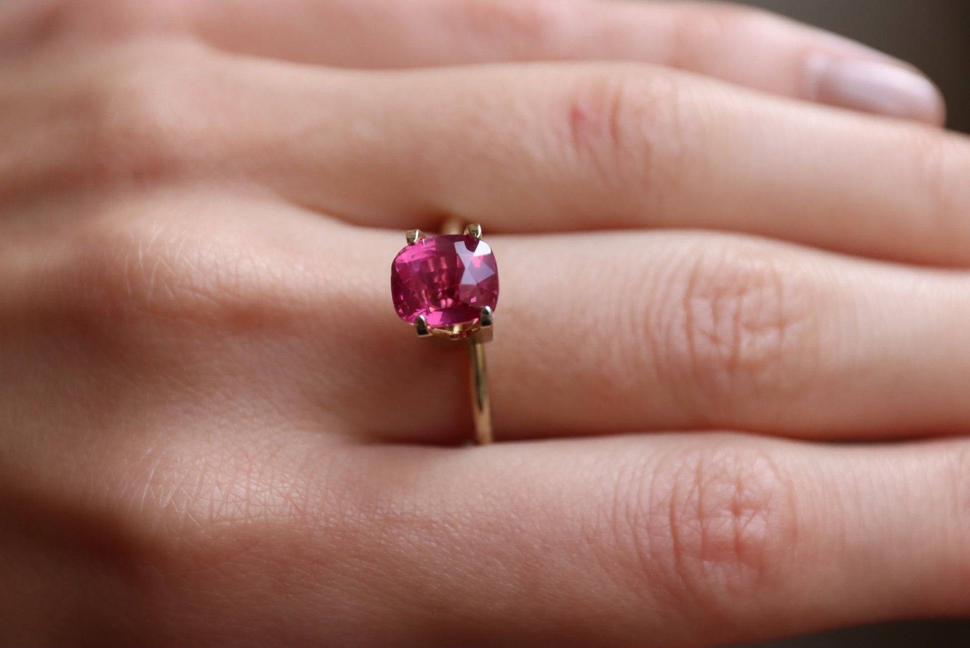 Gros plan sur une main ornée du Saphir Rose de Bonnot Paris, une bague en or ornée d'une pierre rose vif facettée de 3,02 carats. Cette pierre capte magnifiquement la lumière, mettant en valeur sa teinte vibrante.