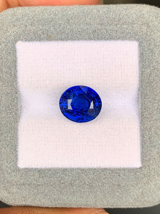 Un Saphir Bleu éclatant de 7,30 carats du Sri Lanka signé Bonnot Paris est présenté sur un coussin gris clair. La pierre taille ronde reflète la lumière, révélant ses teintes bleu profond. Le coussin est tenu entre les doigts pour souligner sa taille impressionnante.