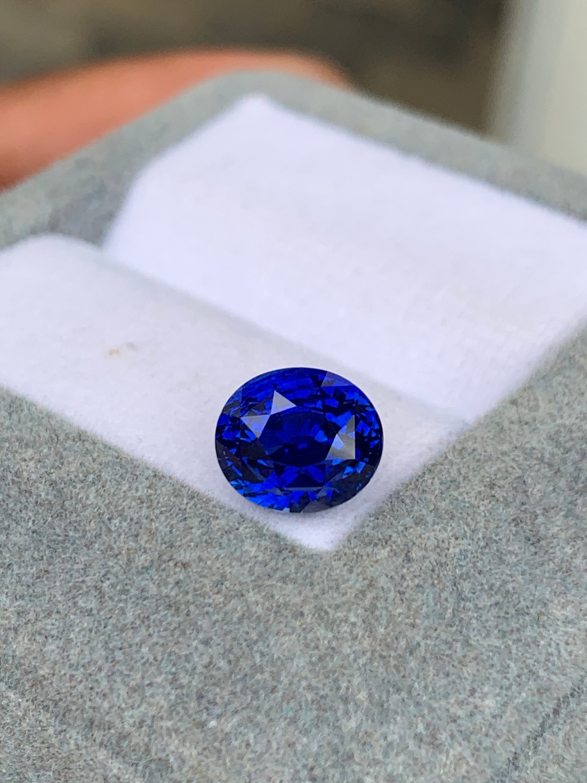 Gros plan sur une pierre précieuse ronde d'un bleu profond de Bonnot Paris, le Saphir Bleu • 3,25 carats, posée sur un écrin doublé de tissu doux. La pierre scintille de mille feux, ses facettes reflétant la lumière comme des pierres précieuses.