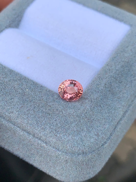 Un Saphir Padparadcha de 1,07 carat de [NOUVEAU] Bonnot Paris, une pierre rose rare, est serti dans une boîte à bijoux ouverte bleu clair, scintillant au centre de son intérieur doux et rembourré.