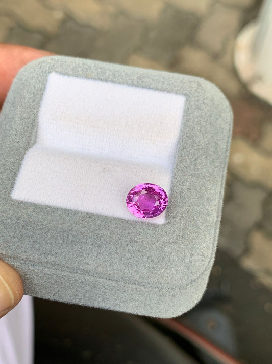 Un Saphir Rose de 2,51 carats de Bonnot Paris repose sur un coussin blanc à l'intérieur d'un coffret à bijoux gris, posé sur un pavé de pierre qui rehausse son allure rose vibrante.