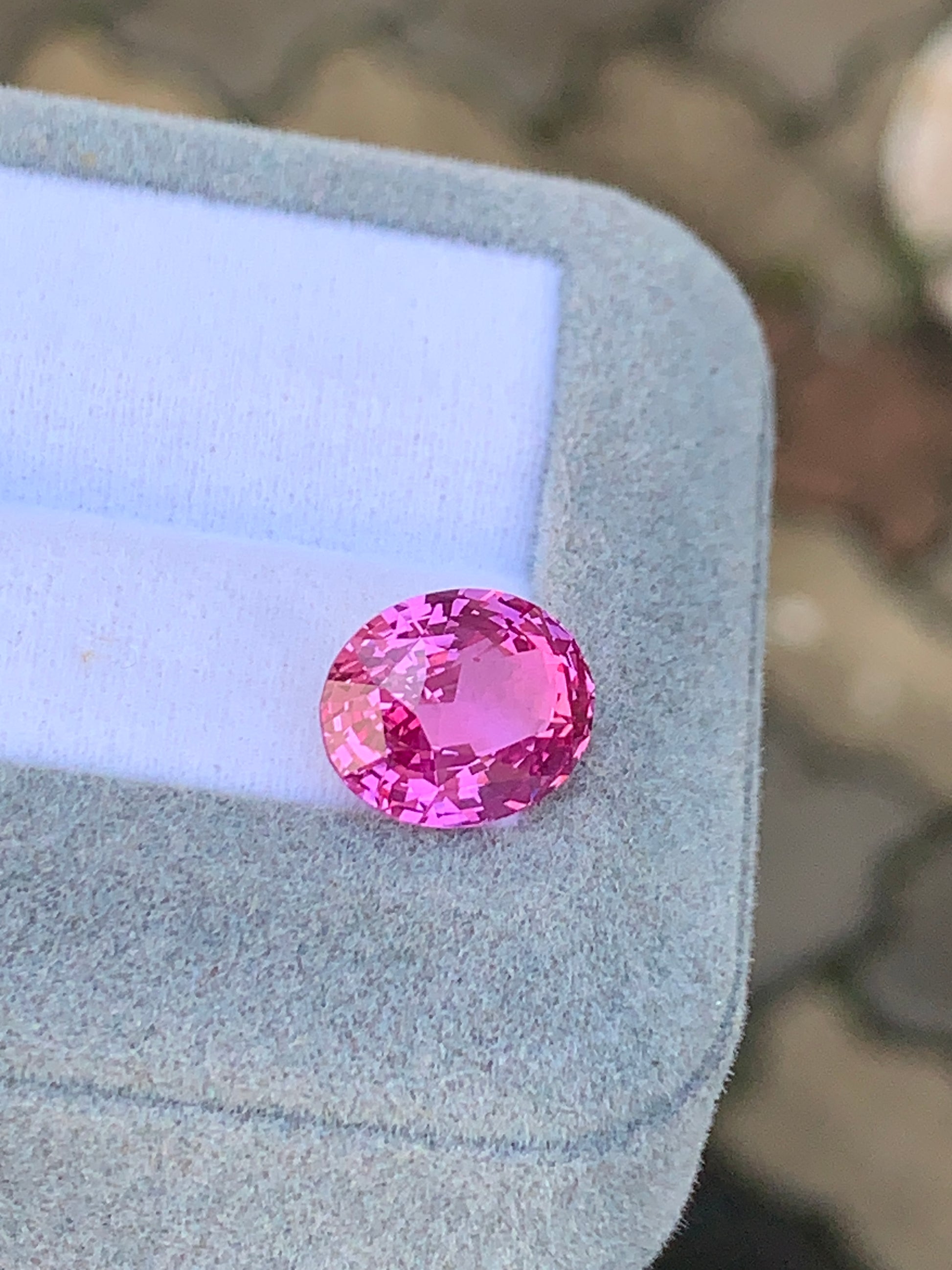 Le Saphir Rose • 7,05ct de [NOUVEAU] Bonnot Paris est élégamment présenté dans une boîte douce gris clair avec un intérieur blanc, sur fond de surface pavée extérieure.
