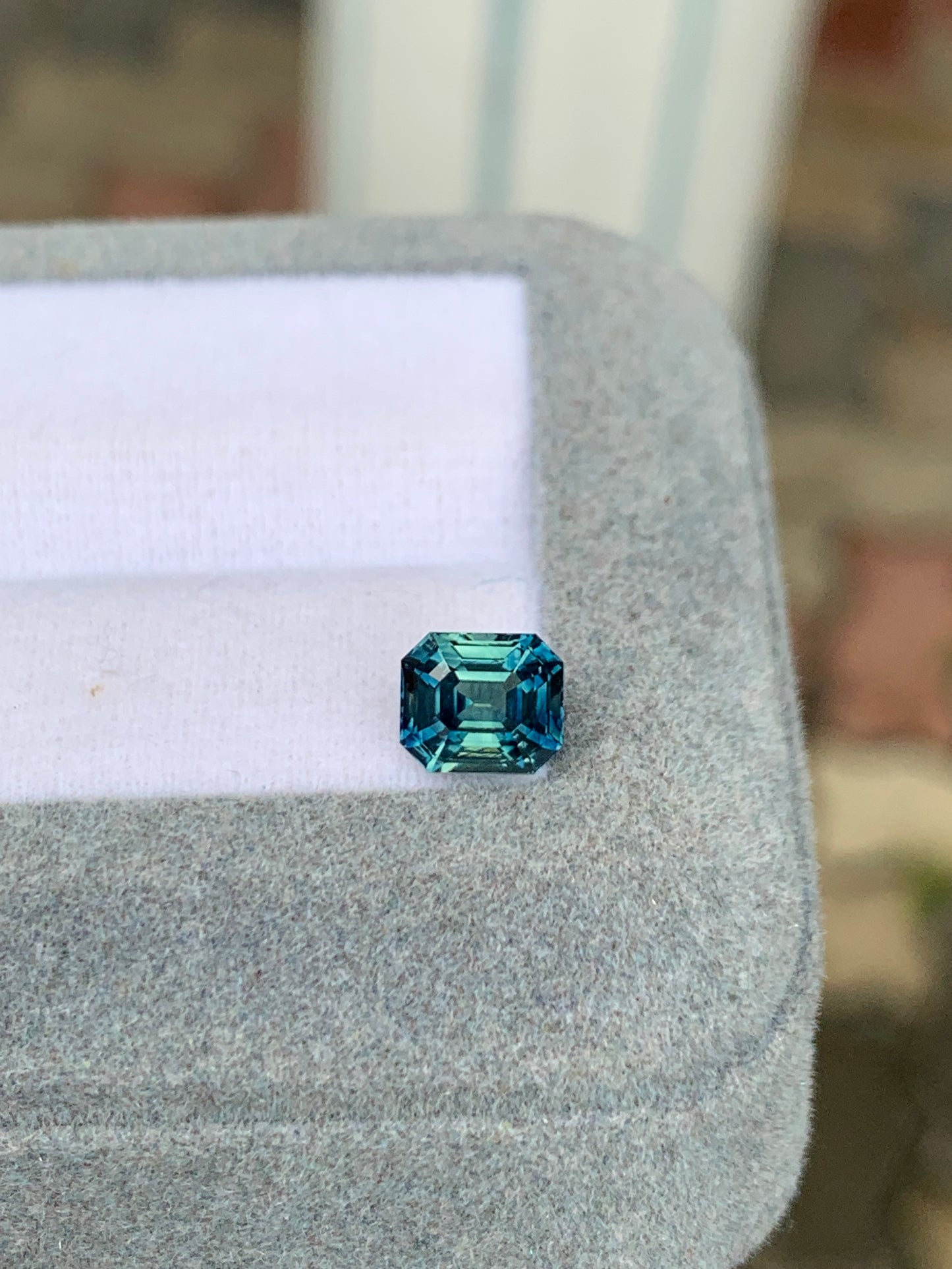 Le Bonnot Paris Saphir Teal • 1,57ct présente une taille émeraude sertie sur une surface grise douce sous la lumière naturelle, avec un fond légèrement flou mettant en valeur cette gemme exceptionnelle.