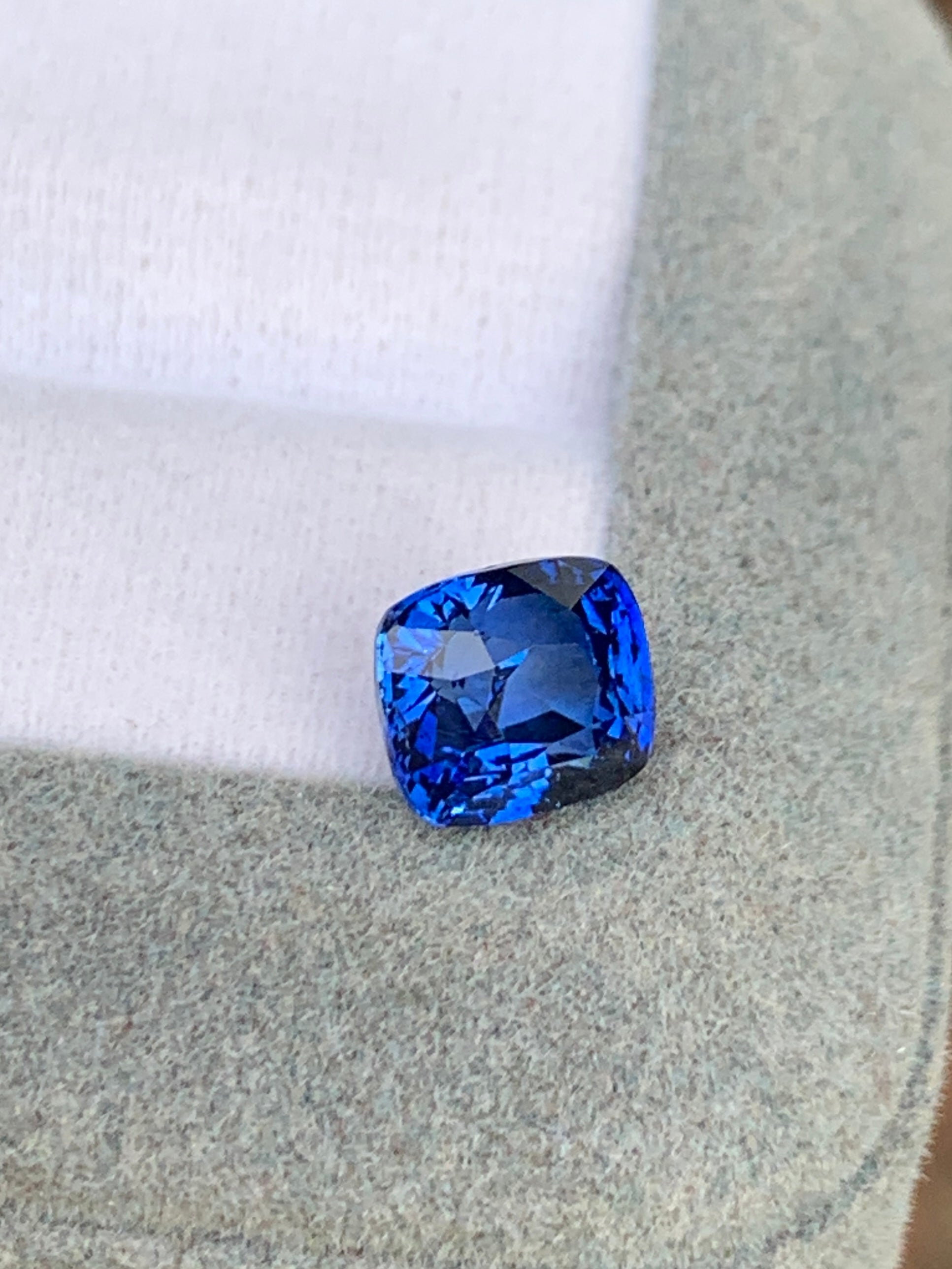 Un saphir bleu éclatant de 3,02 carats de Bonnot Paris, taille coussin, repose sur une surface grise douce sur fond blanc. Cette pierre précieuse exquise reflète magnifiquement la lumière et crée de superbes motifs.