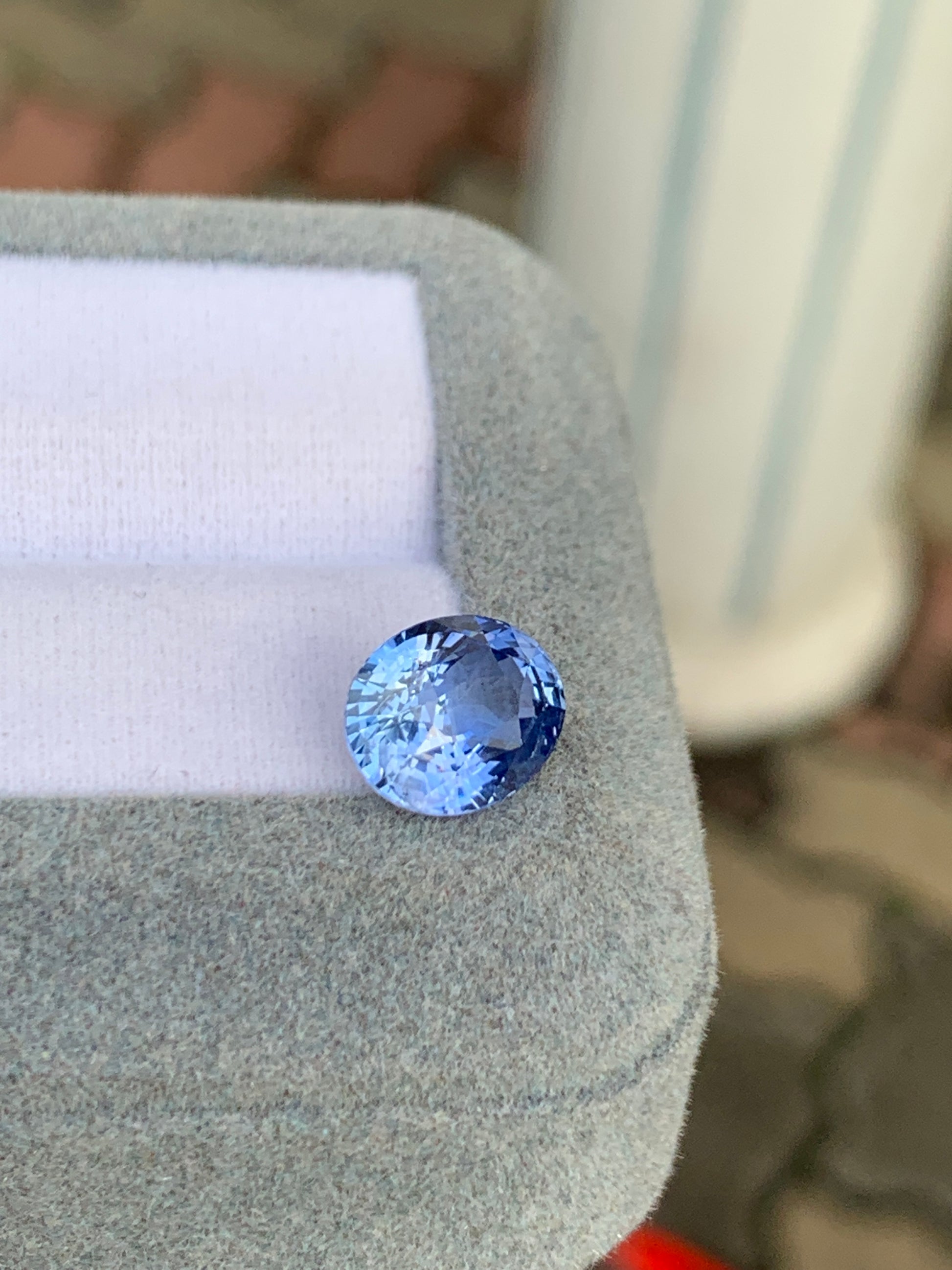 Un Saphir bleu facetté de 4,02 carats de Bonnot Paris repose élégamment sur un coussin gris doux avec un insert blanc. Le flou des colonnes blanches et du pavé de briques rehausse l'attrait de cette pierre précieuse exquise.