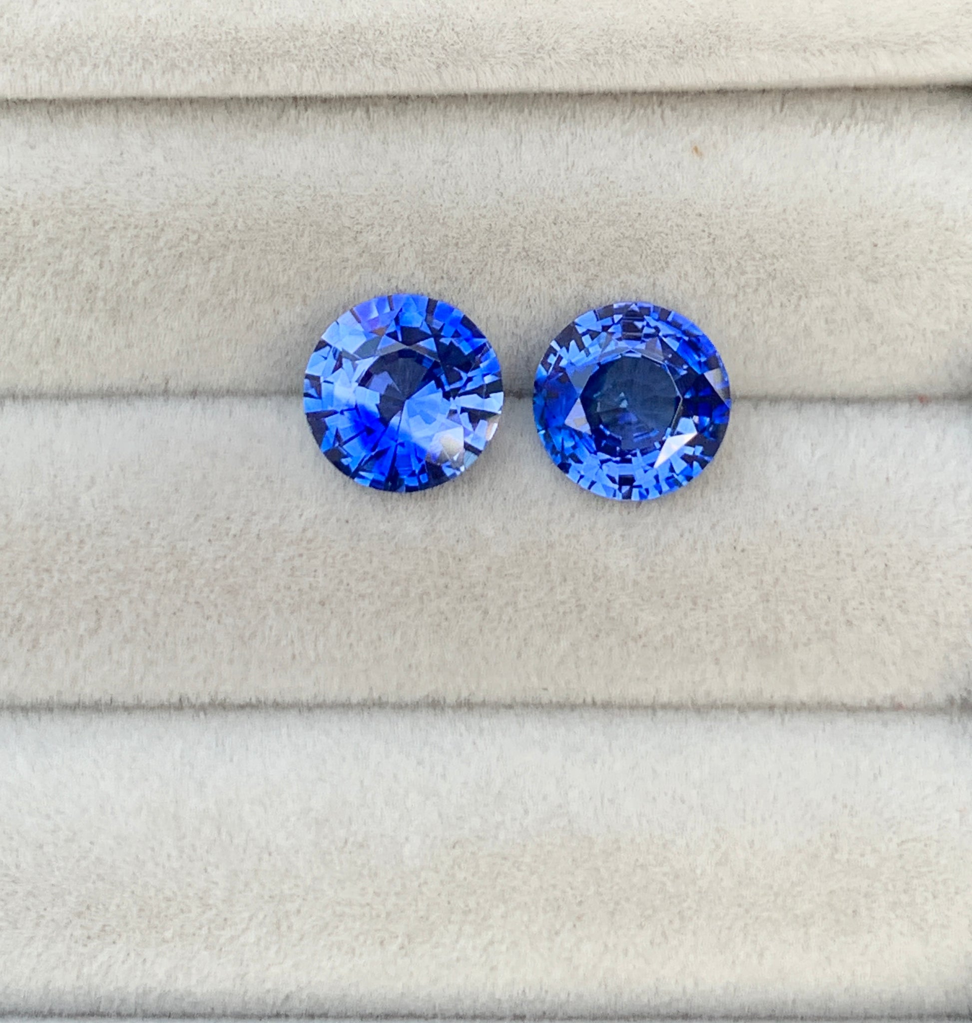 Deux pierres précieuses saphir bleu de 4,90 carats de [NOUVEAU] Bonnot Paris reposent sur un tissu gris clair, mettant en valeur leur couleur vibrante et leurs facettes complexes, incarnant l'attrait des pierres précieuses haut de gamme.