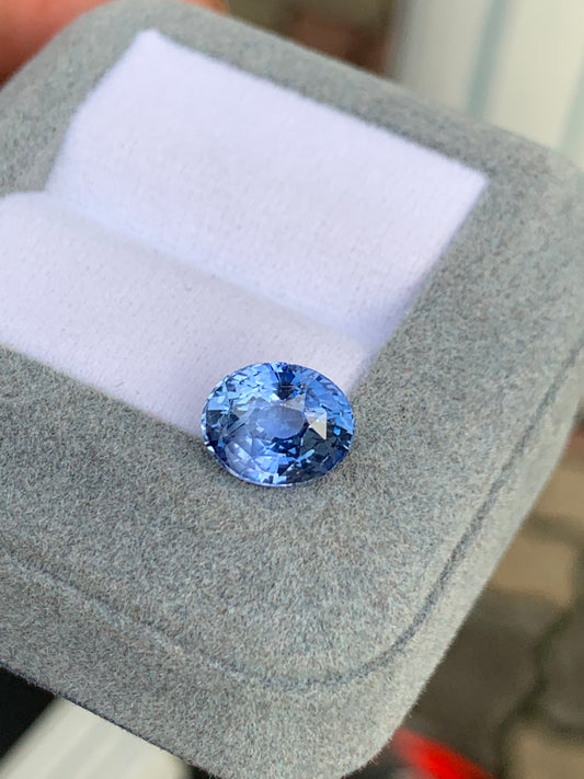Gros plan sur la pierre précieuse Saphir bleu • 4,02ct de Bonnot Paris, scintillante dans un écrin gris à l'intérieur blanc, sur un fond légèrement flou.