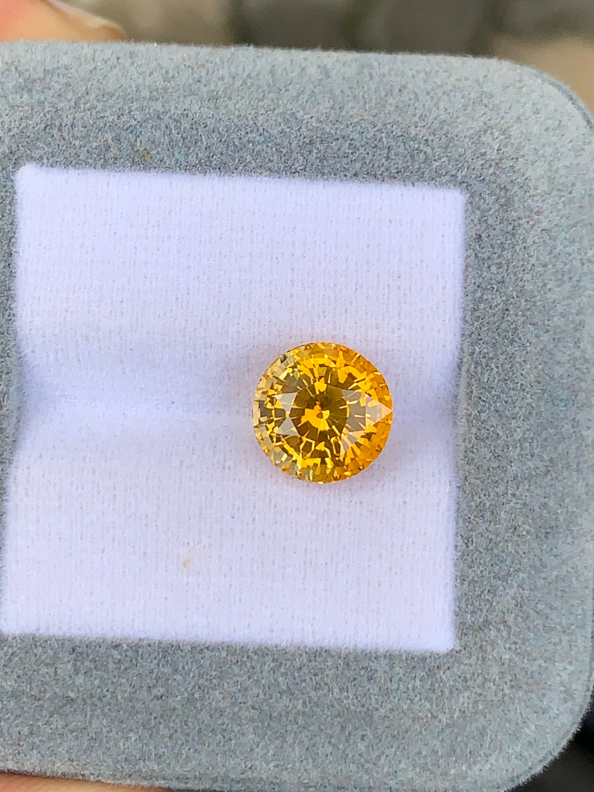 Un Saphir jaune rond • 5,75ct de [NOUVEAU] Bonnot Paris scintille sous la lumière dans un écrin à bijoux gris et blanc.