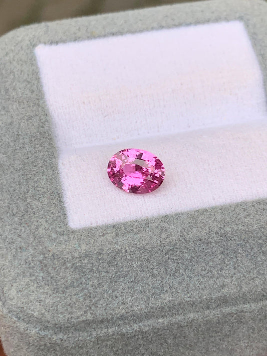 Un Saphir rose de 1,13 carat de la maison Bonnot Paris [NOUVEAU] est élégamment présenté dans un écrin gris clair texturé. La pierre taille ovale capte magnifiquement la lumière, sa couleur vibrante étant sublimée par le contraste du fond qui souligne son éclat.