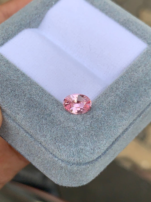 Le Saphir rose • 1,2ct de Bonnot Paris est élégamment présenté dans un écrin en velours gris, sa teinte rose scintillant sur un fond délicatement flou.