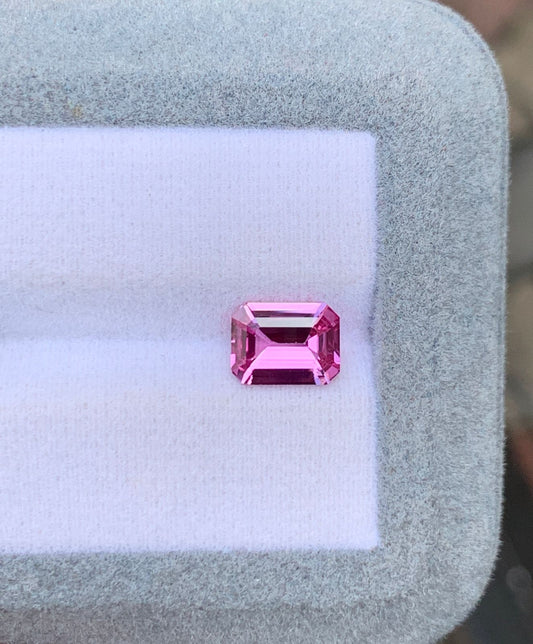 Un Saphir rose taille émeraude étincelant de 2,03 ct de Bonnot Paris est présenté sur un coussin blanc bordé de gris clair. Ses facettes captent la lumière, soulignant sa clarté et sa couleur vive, typiques des pierres précieuses.