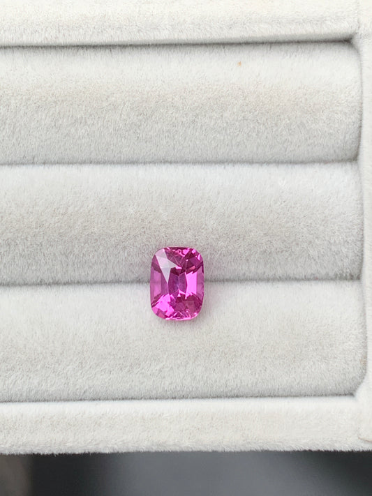 Un Saphir rose éclatant de 2,10 carats, taille coussin, signé Bonnot Paris, repose dans un écrin gris clair strié. Ses facettes captent la lumière, révélant de multiples nuances de rose.