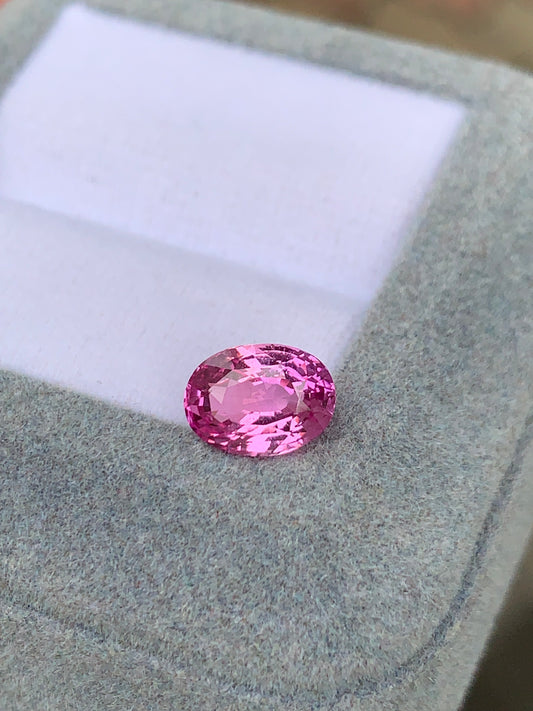 La pierre précieuse Saphir rose • 2,2 ct de Bonnot Paris est un bijou ovale rose facetté et réfléchissant la lumière posé sur une surface grise texturée, peut-être une boîte à bijoux avec un intérieur blanc.