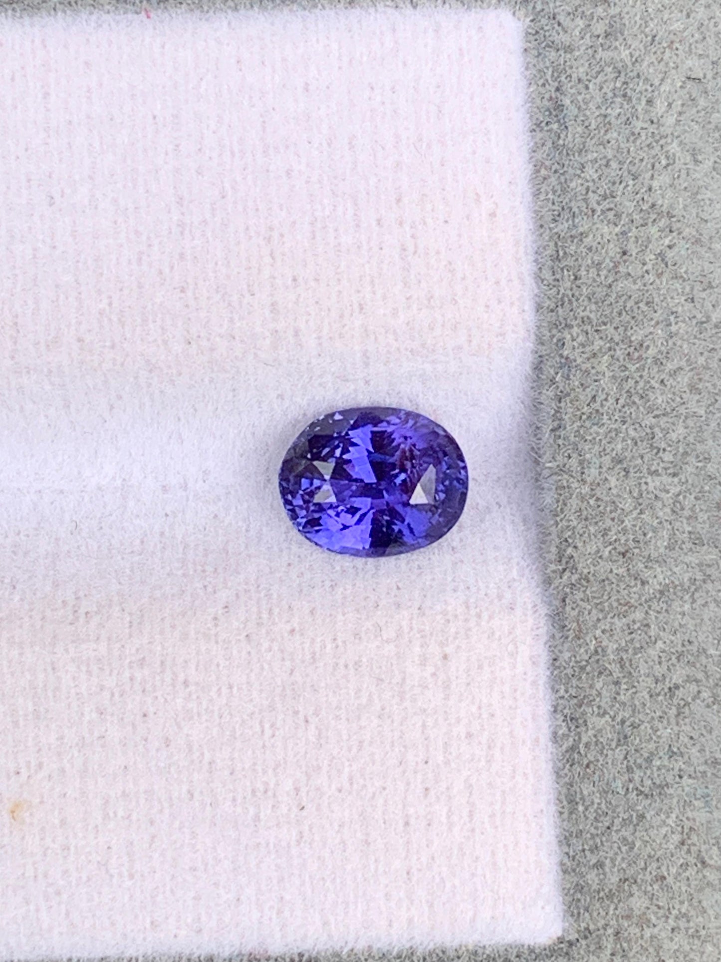 Le Saphir violet • 1,10ct de [NOUVEAU] Bonnot Paris, une exquise gemme ovale du Sri Lanka, repose sur une surface texturée grise et blanche, reflétant la lumière pour révéler ses facettes étonnantes et son allure intemporelle.
