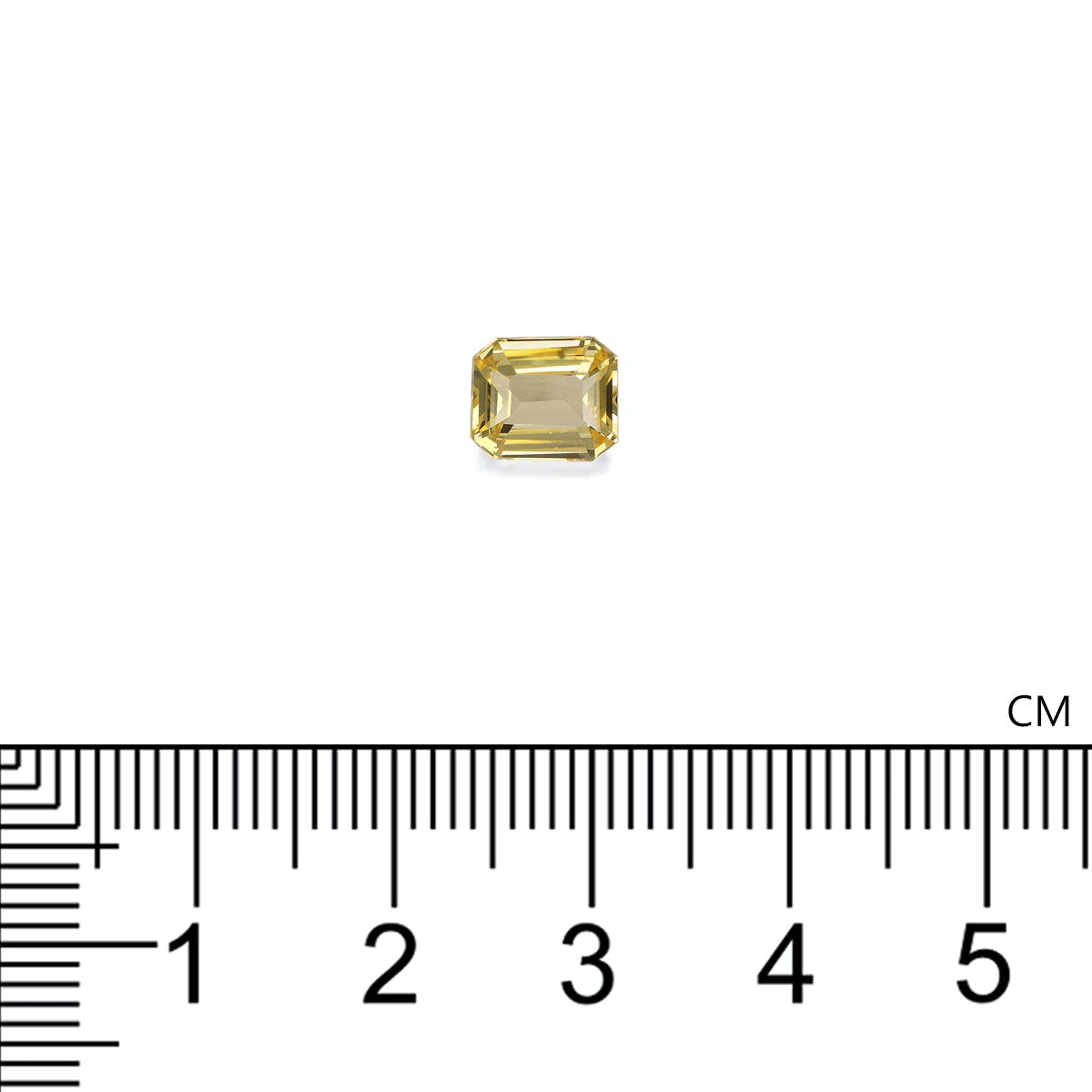 Le Saphir Jaune · 2,05ct de Bonnot Paris, une petite pierre précieuse jaune taille émeraude, est placé sur une surface blanche près d'une règle centimétrique, indiquant que la taille de la pierre est d'environ 0,8 cm.