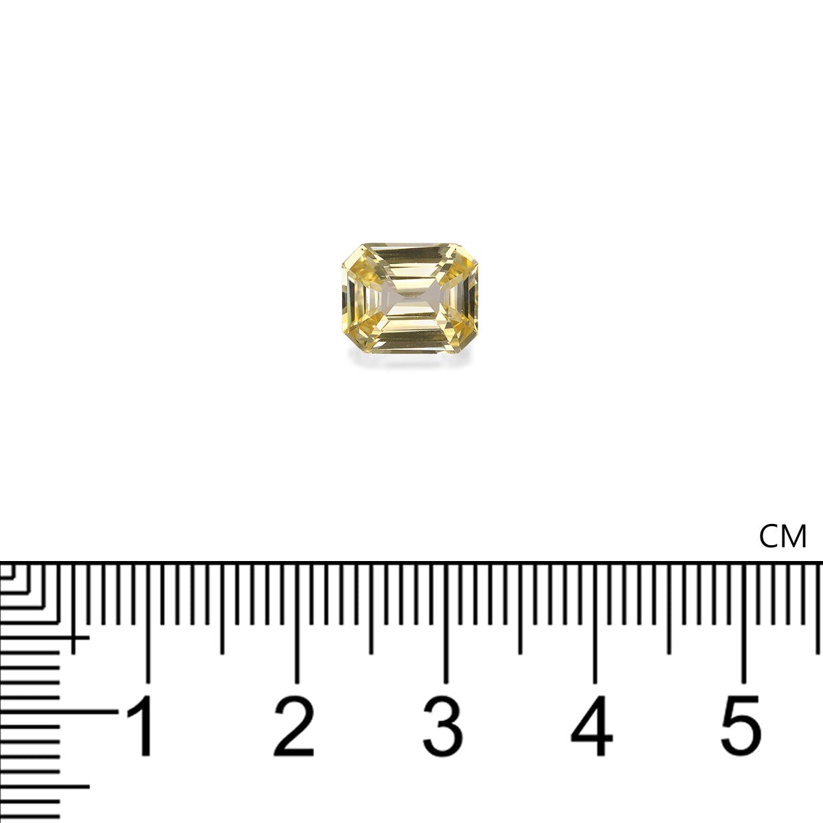 Le Saphir Jaune · 3,06 carats de Bonnot Paris est une petite pierre jaune rectangulaire sertie sur un fond blanc uni. Une règle graduée en centimètres sous la pierre indique son diamètre d'environ 1 centimètre.